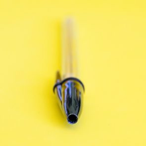 A black pen lies idle on a bright yellow background, emphasizing its pointed tip.