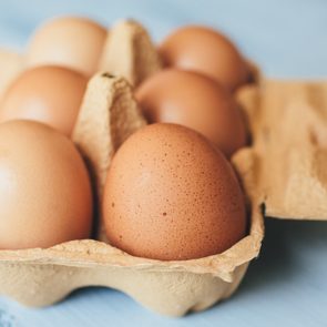 Brown eggs resting in a cardboard carton on a light blue surface.