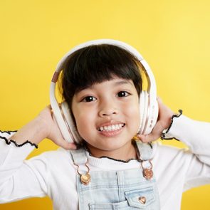 Child wears white headphones, smiling broadly against a bright yellow background.