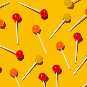 Lollipops scattered randomly, featuring red, orange, and yellow colors, against a bright yellow background.
