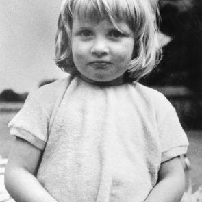 Child stands calmly, hands clasped, wearing a light shirt outdoors on a cloudy day.