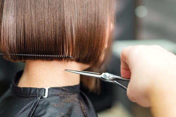 Haircutting scissors trim straight brown hair in a salon, with hair clips securing the section.