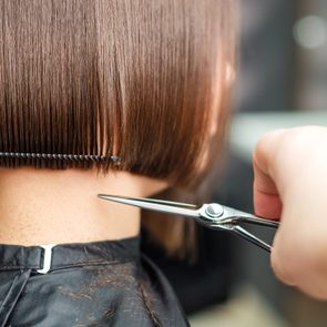 Haircutting scissors trim straight brown hair in a salon, with hair clips securing the section.