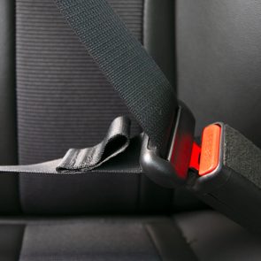 A seatbelt clicks into a red-labeled buckle in a car's dark interior. The buckle has the word 