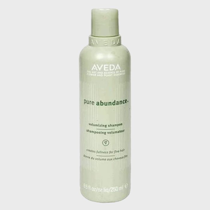 A green Aveda volumizing shampoo bottle stands upright on a plain background with text detailing product benefits for fine hair.
