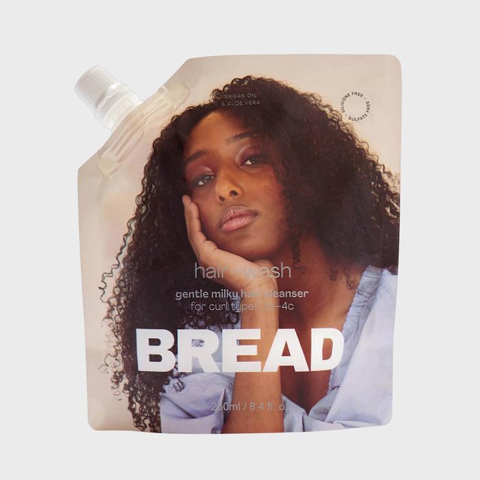 Hair cleanser pouch features a woman resting her face on her hand; marketed for curly hair types 3a-4c. Contains argan oil and aloe vera.