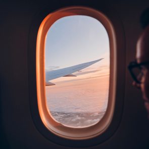 Airplane wing extending through window during sunset, viewed from passenger seat with clouds and sky in the background.