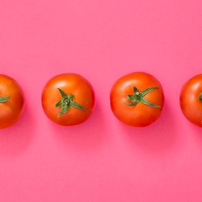 Four tomatoes lie in a row against a bright pink background.