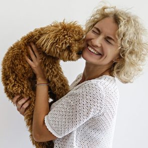 A woman hugs a curly-haired dog affectionately against a plain white background.