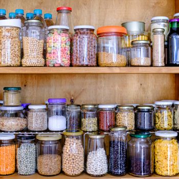 Jars store various dry foods, such as grains and spices, neatly arranged on wooden pantry shelves.