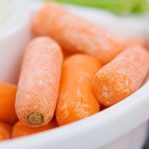 Baby carrots resting in a white bowl, close-up, with a blurred background.