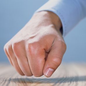 A clenched fist knocks on a wooden surface, surrounded by a blue background.