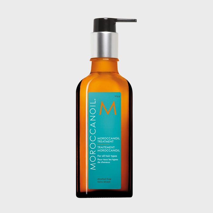 A brown bottle with a pump dispenses hair treatment, labeled with blue and orange text, against a plain background.