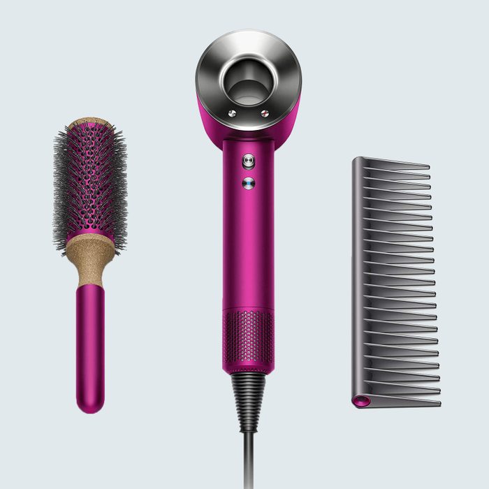Hairdryer positioned vertically, flanked by a round brush on the left and a comb on the right, set against a plain background.