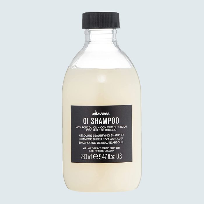 A clear bottle with black cap contains Davines OI Shampoo, featuring Roucou oil. The context is a plain light gray background.