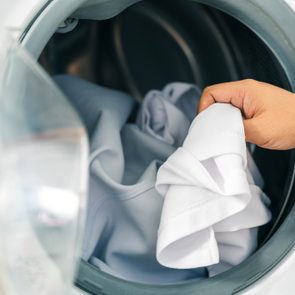 A hand removes white clothes from a front-loading washing machine, indicating laundry completion.