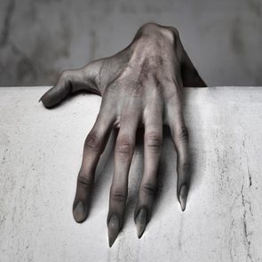 A pale, clawed hand grips a slightly dirty white surface against a blurred, gray background.