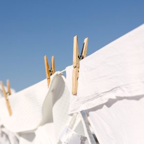 Clothespins secure white fabric on a clothesline against a clear blue sky.