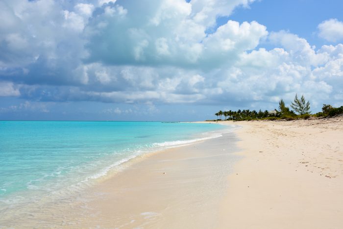 Beach stretches alongside turquoise water, bordered by palm trees under a partly cloudy blue sky.