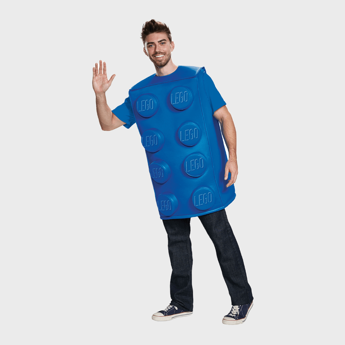 A person wears a blue LEGO brick costume, waving, standing against a plain background.
