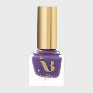 Purple nail polish sits in a rectangular glass bottle with a golden cap, against a plain gray background.