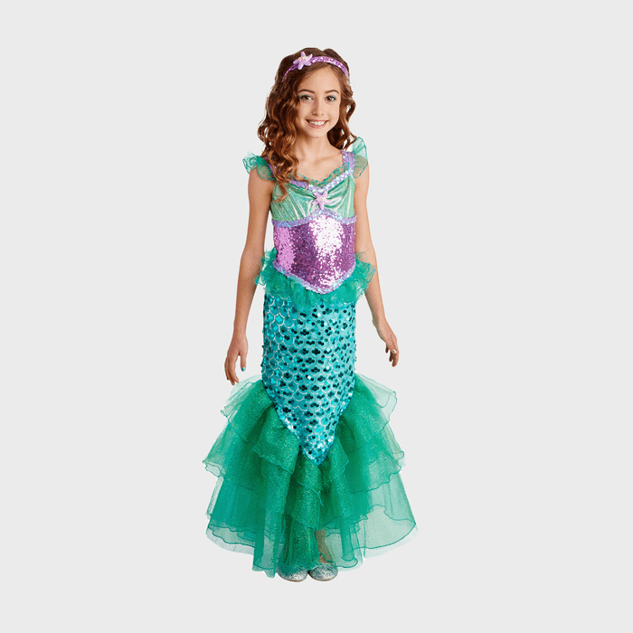 Young girl smiles, wearing a shimmering mermaid costume with green and purple sequins, standing against a plain white background.
