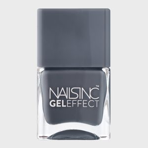 A square bottle of gray nail polish sits still on a plain, light background. Text on the bottle reads 
