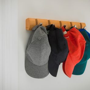 Baseball caps hang from wooden pegs on a wall, organized in a row with varying colors, including gray, black, red, and blue.
