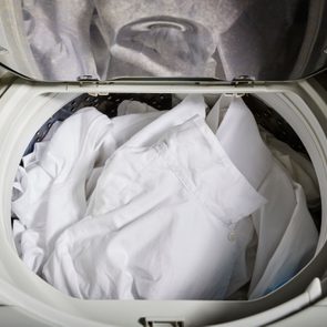 White shirts lie inside an open washing machine drum, ready for washing, in a laundry room setting.