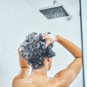 Person washing hair, lathering shampoo, in a tiled shower area.
