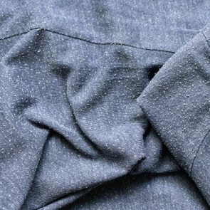 Blue fabric with white speckles lies crumpled, displaying an intricate texture in natural lighting.