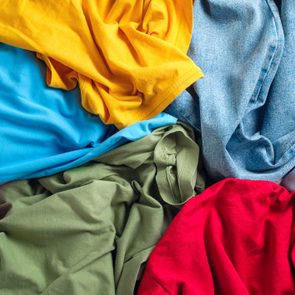 Clothes lie in a pile displaying various colors, including yellow, blue, green, red, and denim, creating a vibrant and mixed arrangement.