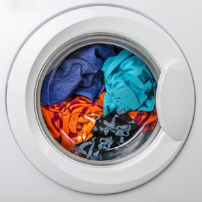 Clothes tumble inside a front-loading washing machine with a circular glass door, surrounded by a white frame.