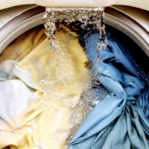 Water pours onto colorful clothes inside a washing machine, creating bubbles in bright lighting.