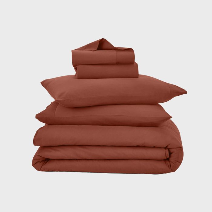 A stack of brown bed linens sits neatly folded against a plain gray background.