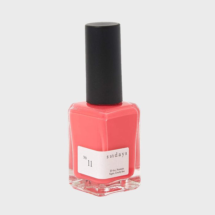 A coral nail polish bottle stands upright against a plain background, labeled 
