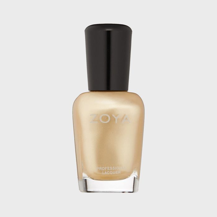 A gold nail polish bottle sits with a black cap against a plain gray background. The label reads 