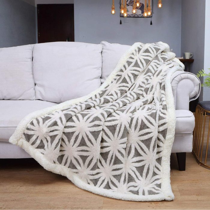Blanket drapes over a light-colored couch, showcasing a geometric pattern in a cozy living room with wooden floor and hanging lights.