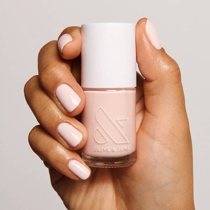 Hand holding a bottle of light pink nail polish, labeled 