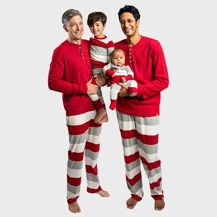 Two adults and two children wear matching red and gray striped pajamas, standing and smiling against a plain background.