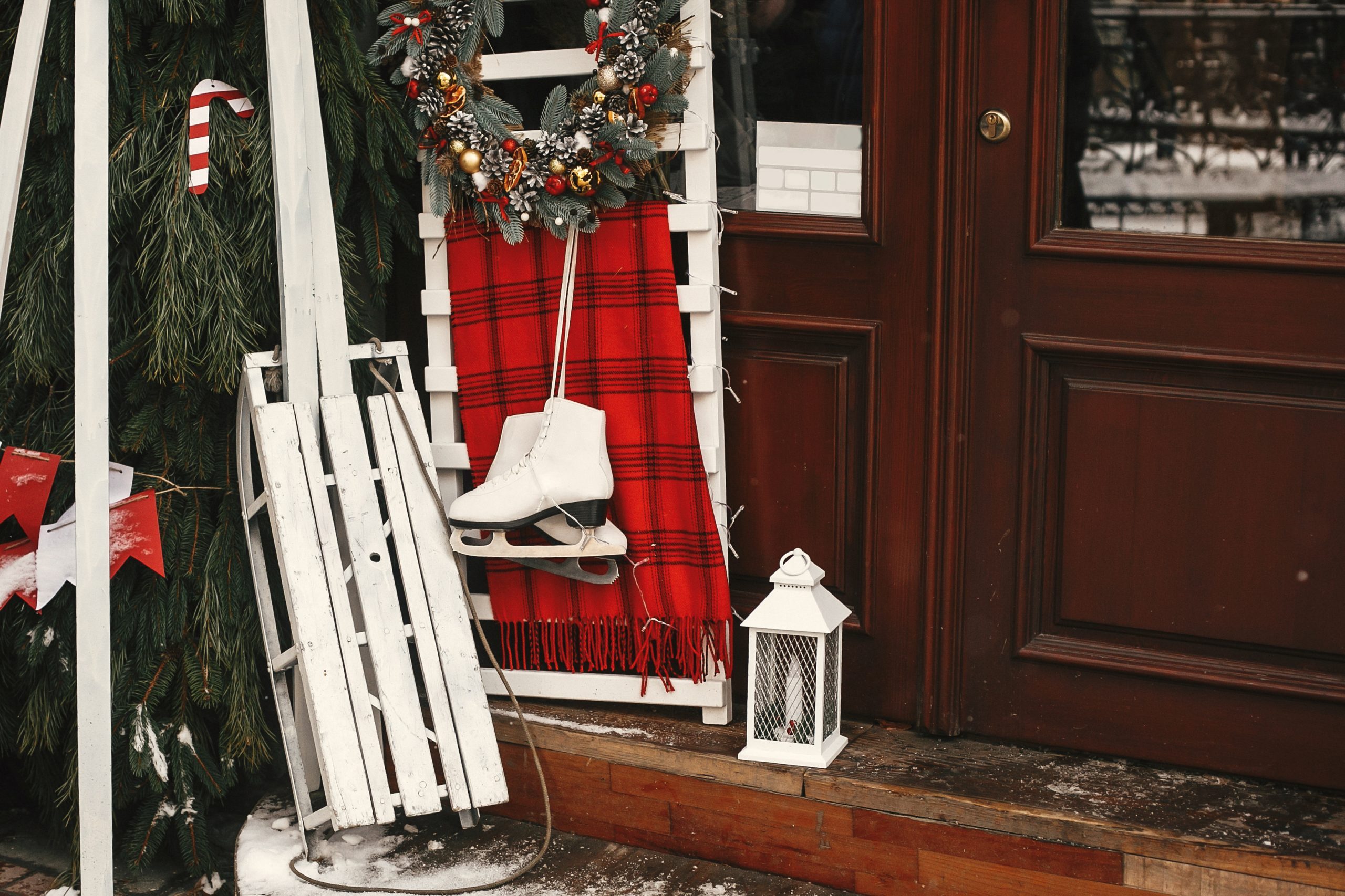 Stylish christmas wreath, white wooden sleigh and ice skate at front of store at holiday market in city street. Christmas street decor.
