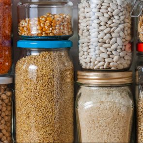 Glass jars containing various grains and cereals are neatly arranged in a pantry, showing vibrant colors and textures.