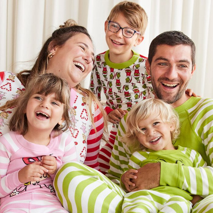 Family smiles, wearing colorful striped pajamas with holiday patterns, sitting together in a cozy, brightly lit room, suggesting a joyful, festive atmosphere.