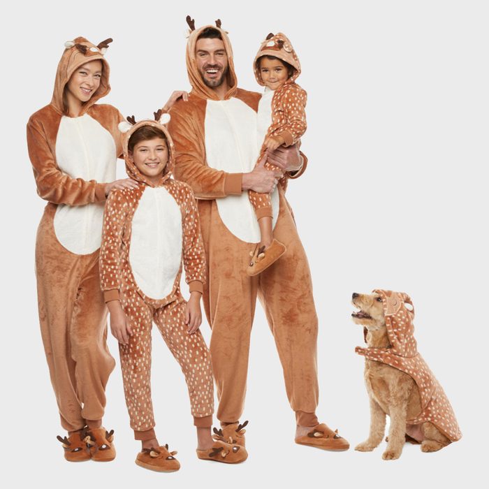 Family wearing brown deer onesies smiling together; a dog dressed similarly sits to their side against a plain background.