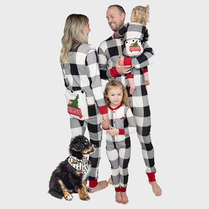 Family wearing matching plaid pajamas, standing together with a small dog. Background is plain. Pajamas have 'TAILGATE' text on pockets.