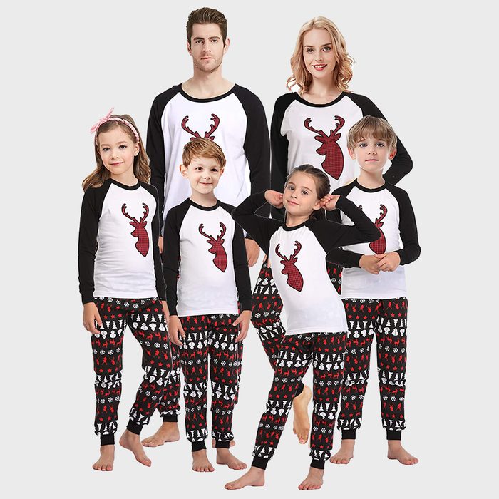 Family wearing matching pajamas with reindeer tops and festive patterned pants, standing together against a plain background.