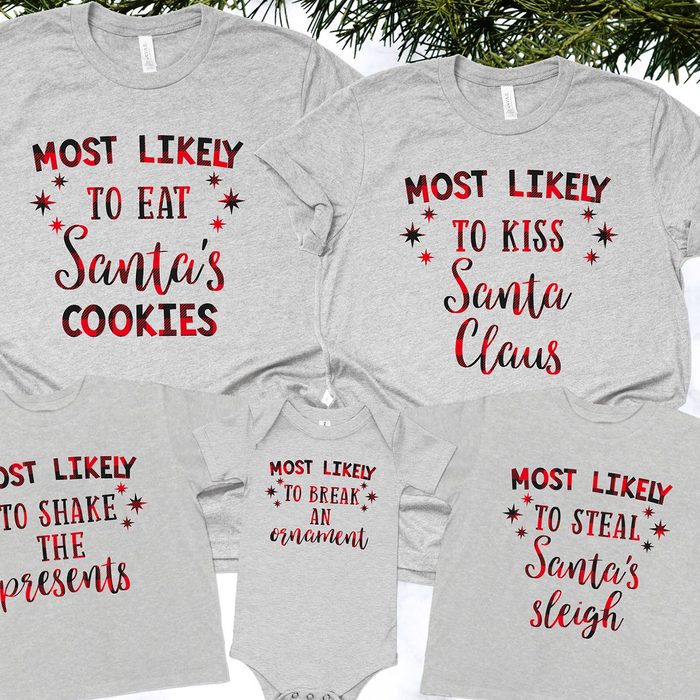 Gray shirts with humorous holiday-themed text on them, surrounded by pine branches; text includes 