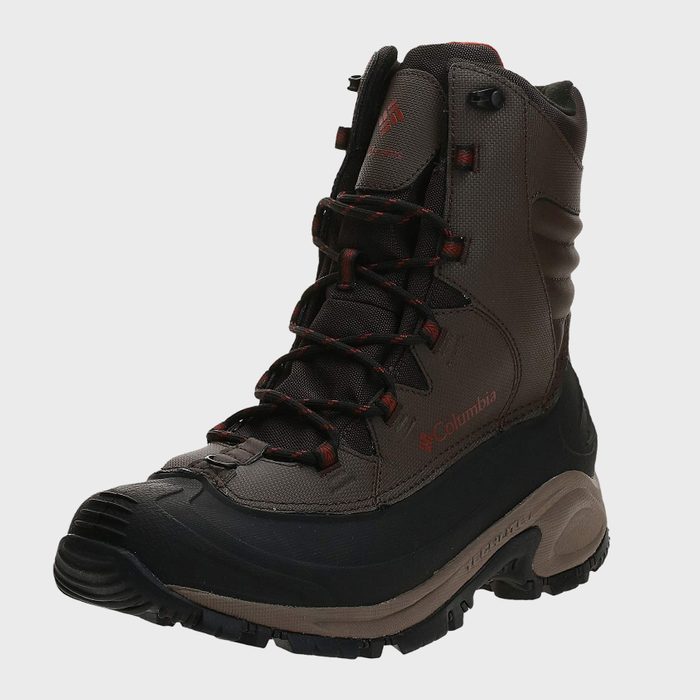 A brown hiking boot stands upright, showcasing its detailed laces and rugged sole against a plain background. 