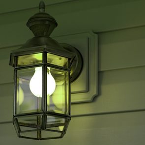 A lantern-style wall light glows, illuminating a wooden exterior wall with horizontal paneling.