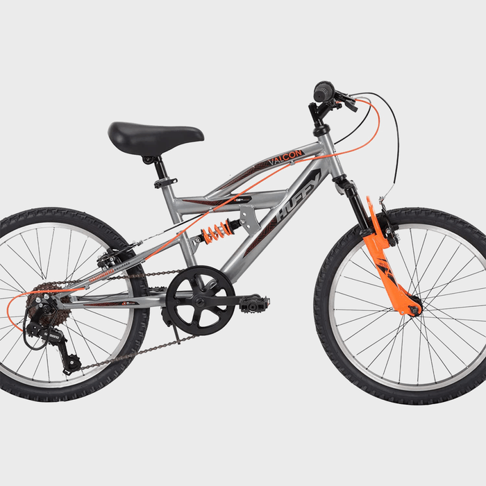 Bicycle stands motionless in a bright setting; features gray and orange frame, full suspension, knobby tires, and labeled 